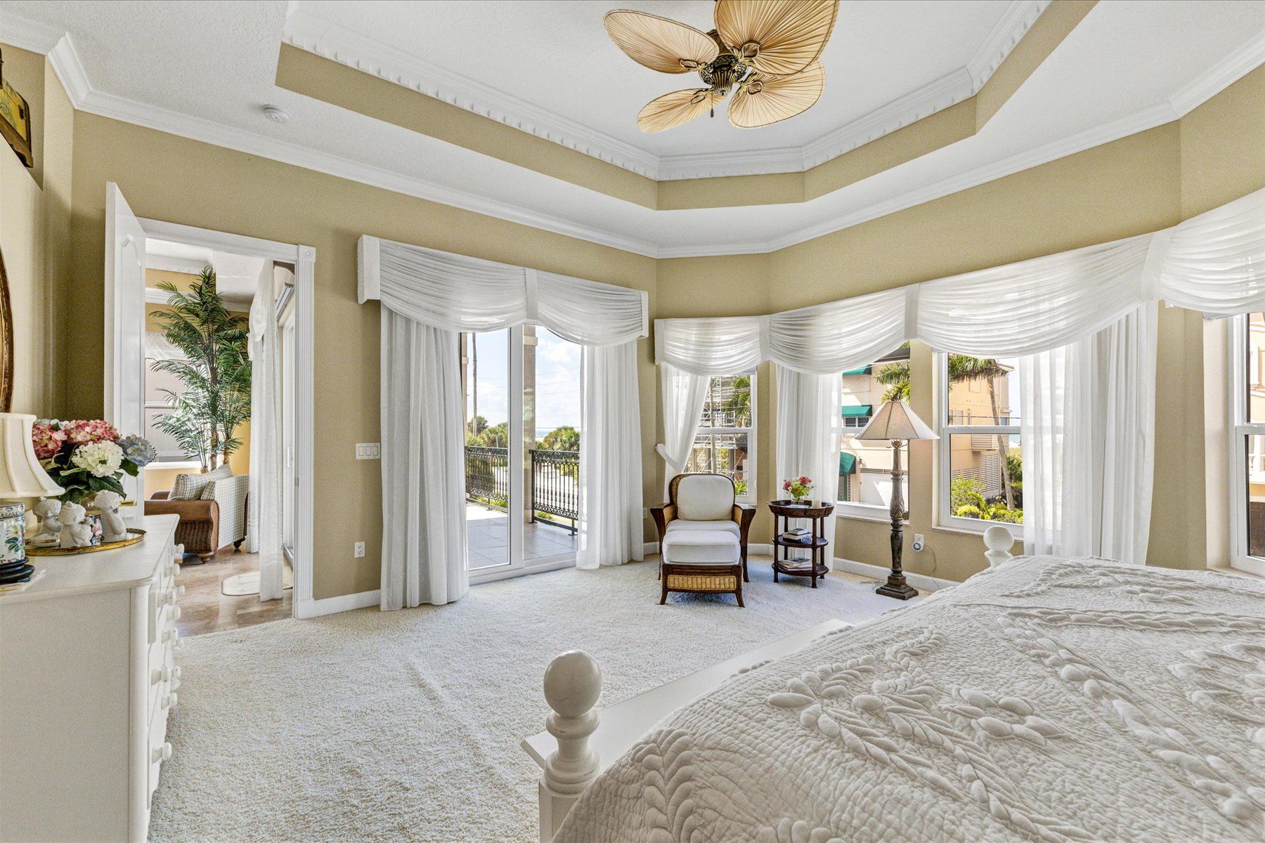 A spacious bedroom with a large bed, a ceiling fan, and a view of the outside balcony.