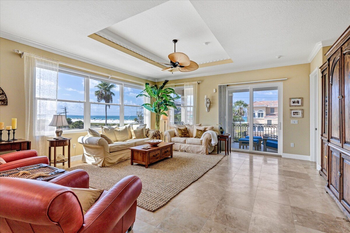 A spacious living room with a large window, a ceiling fan, and a view of the beach.