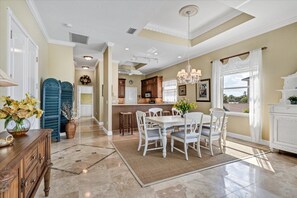 A spacious kitchen with a dining area, featuring a large island, white cabinetry, and a view of the outdoors. - Ocean Vue By Beachside Management (Siesta Key)