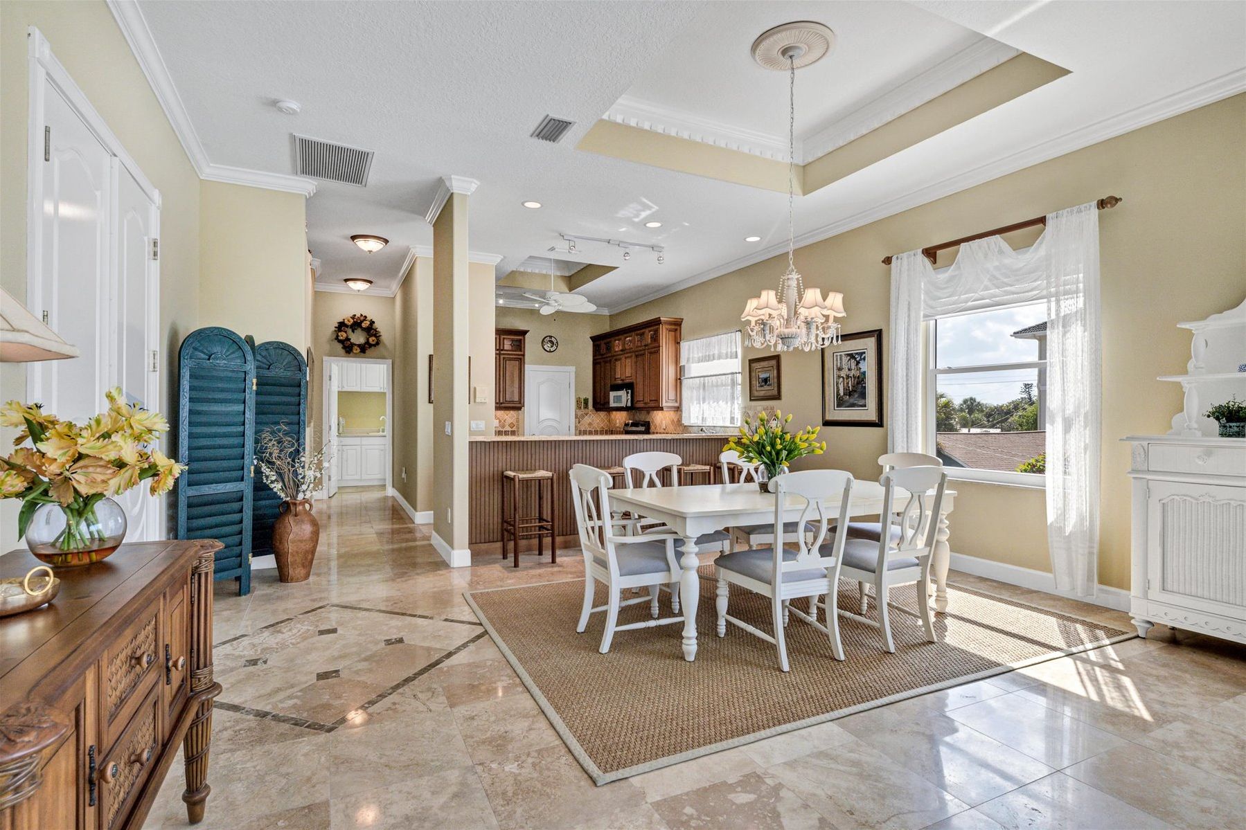 A spacious kitchen with a dining area, featuring a large island, white cabinetry, and a view of the outdoors.