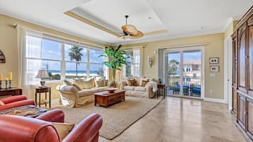 Un salon spacieux doté d’une grande fenêtre, d’un ventilateur de plafond et offrant une vue sur la plage.