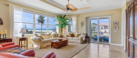 A spacious living room with a large window, a ceiling fan, and a view of the beach.