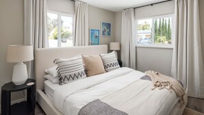 Een slaapkamer met een bed, twee nachtkastjes, een kroonluchter en gordijnen.