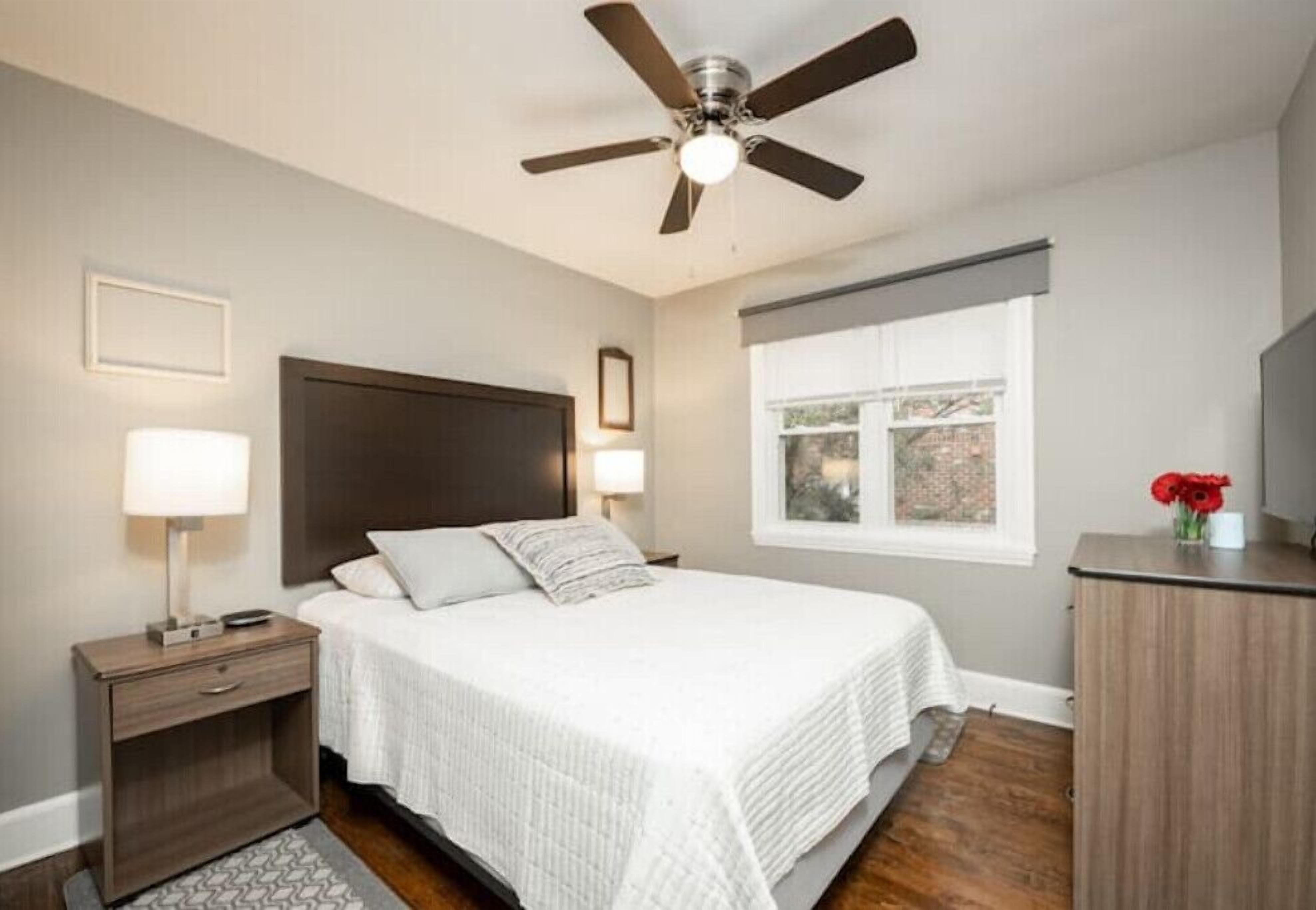 Une chambre à coucher comprenant un lit, des tables de chevet, un bureau, un ventilateur de plafond et une fenêtre donnant sur un beau paysage.