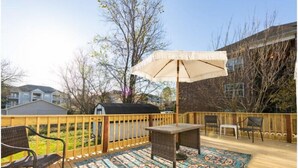 Eine Terrasse mit Teppichmuster, einem Tisch, Stühlen und einem Grill.