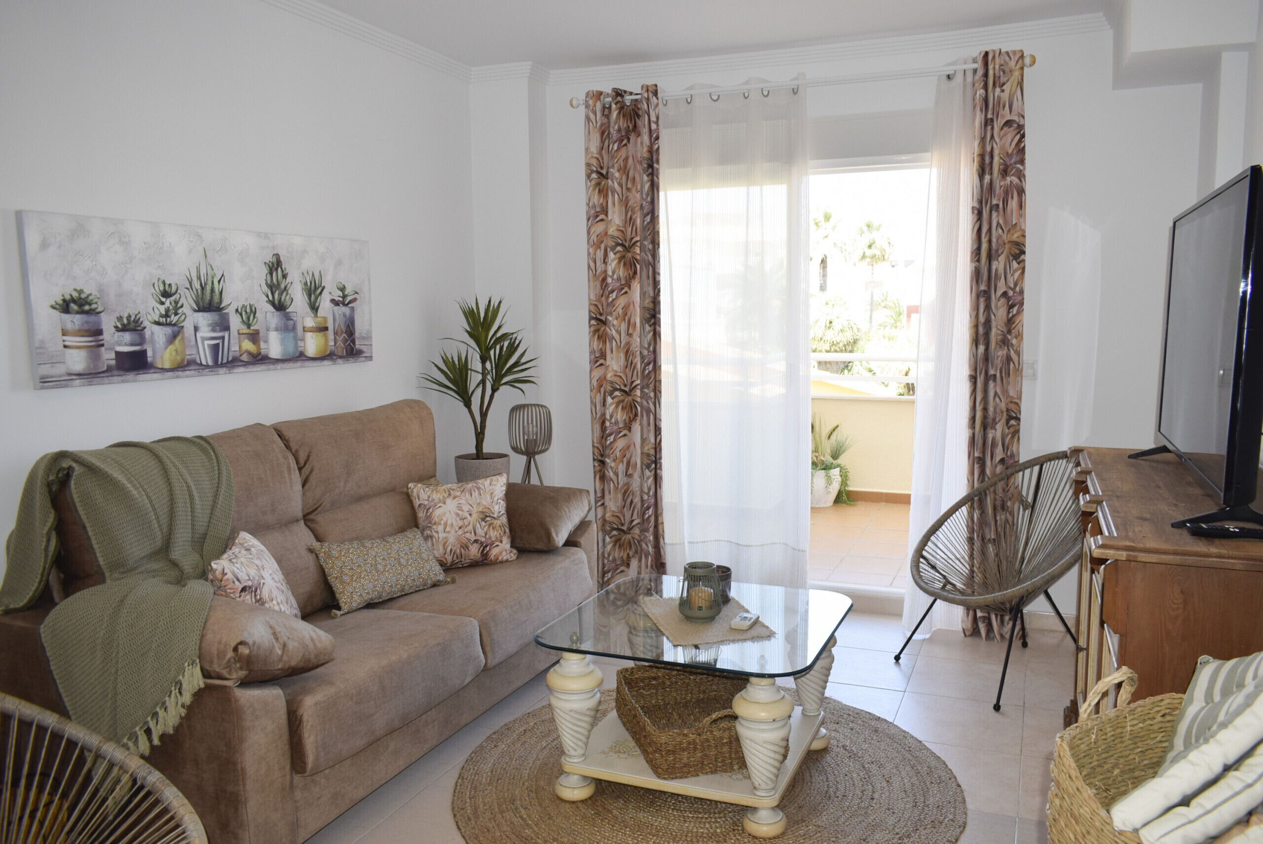 A living room with a glass coffee table, a sofa, a wicker chair, and a television.