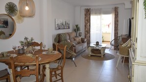 Ein Essbereich mit Holztisch und Stühlen, einer Couch und einem Fernseher im Hintergrund.