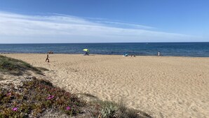 Ein sandiger Strand mit blauem Himmel, einigen Personen und einem gelben Sonnenschirm.