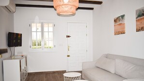 A room with a white sofa, two white round tables, a television, and a door with a window.