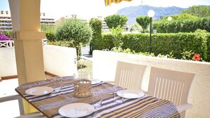 A table set for two with a striped tablecloth, white chairs, and a view of a landscaped garden and mountains in the background.