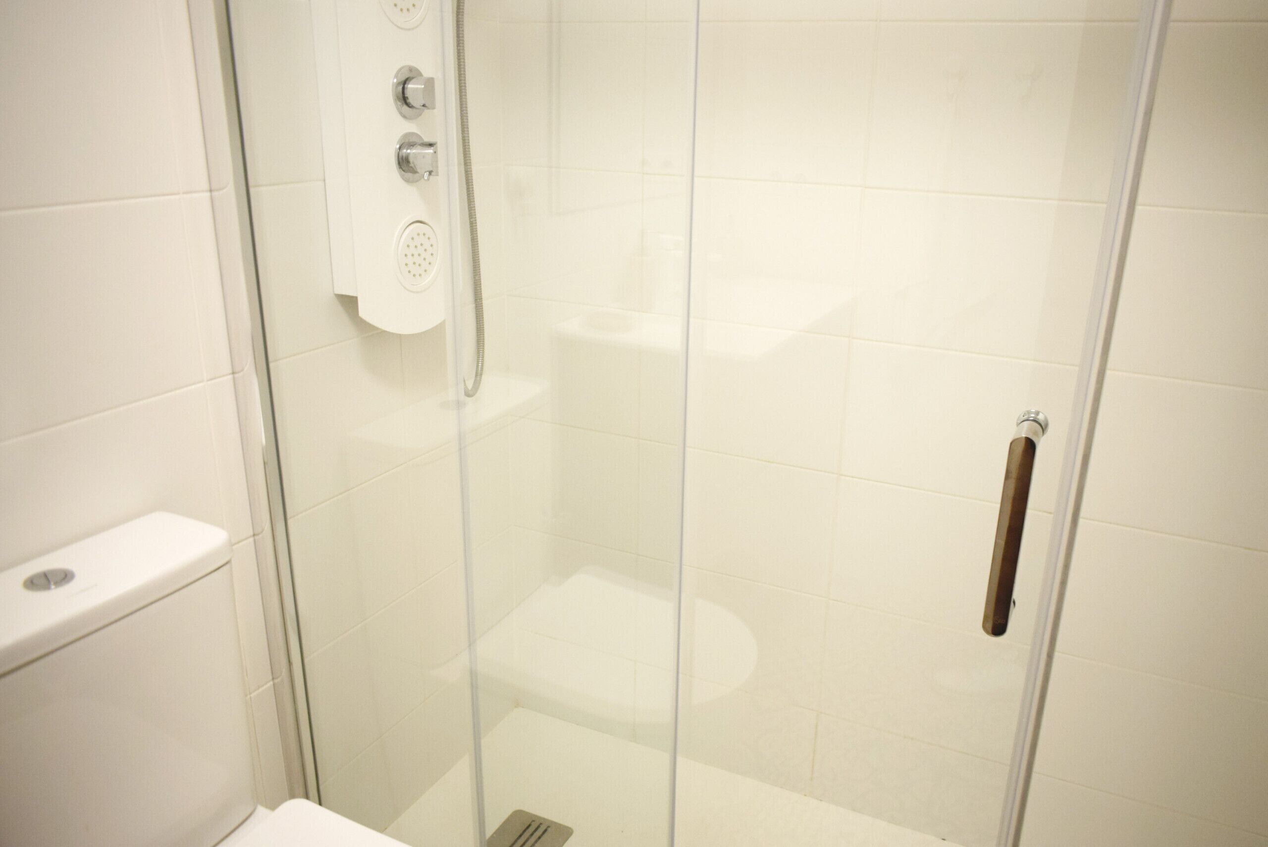 A glass-enclosed shower stall with a toilet and a towel rack.