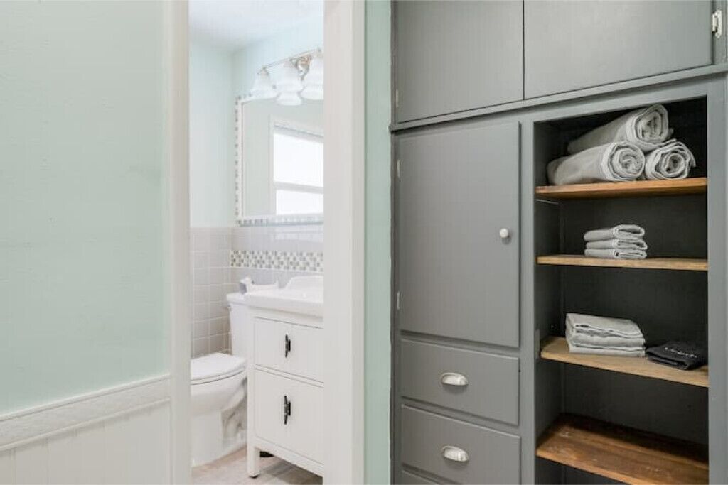 A bathroom with a white toilet, a white sink, and a grey wardrobe with shelves holding folded towels.