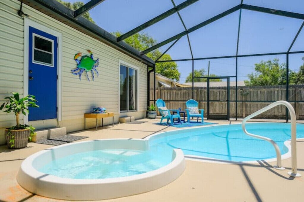 Zona de piscina exterior techada con jacuzzi, sillas de descanso y una casa con puerta azul y decoración de cangrejo.