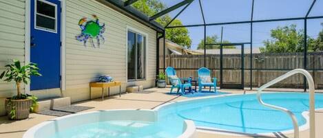 Zona de piscina exterior techada con jacuzzi, sillas de descanso y una casa con puerta azul y decoración de cangrejo.