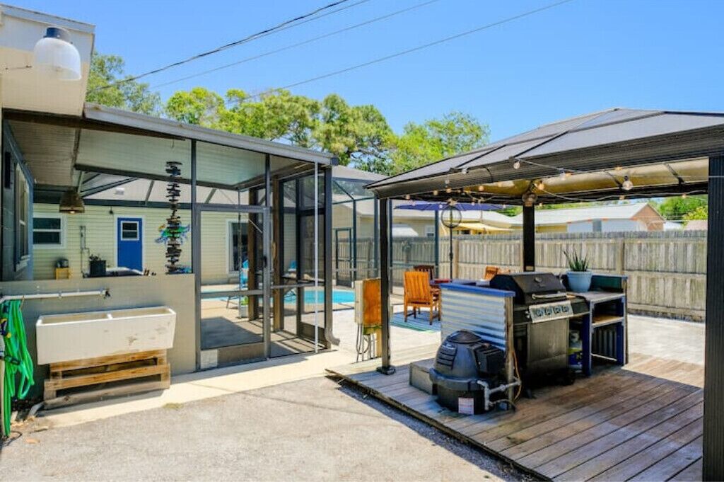 Een modern buiten terras met glazen omheining, een barbecuehoek en een zwembad.