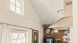 A compact kitchen with a wooden ceiling, a black refrigerator, and a countertop with various appliances. - The Arrow Cottage (Bend)