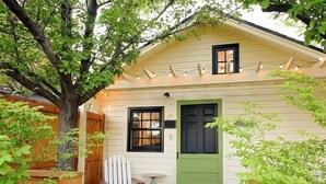 A small, single-story house with a green door and a white chair outside. - The Arrow Cottage (Bend)