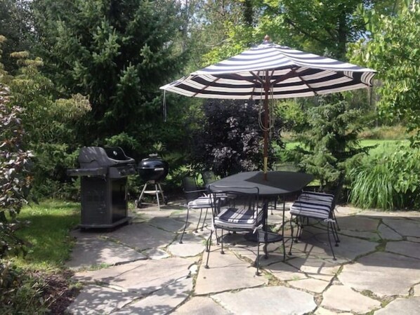Relax in a serene outdoor setting surrounded by lush greenery and trees, with a grill and dining area.