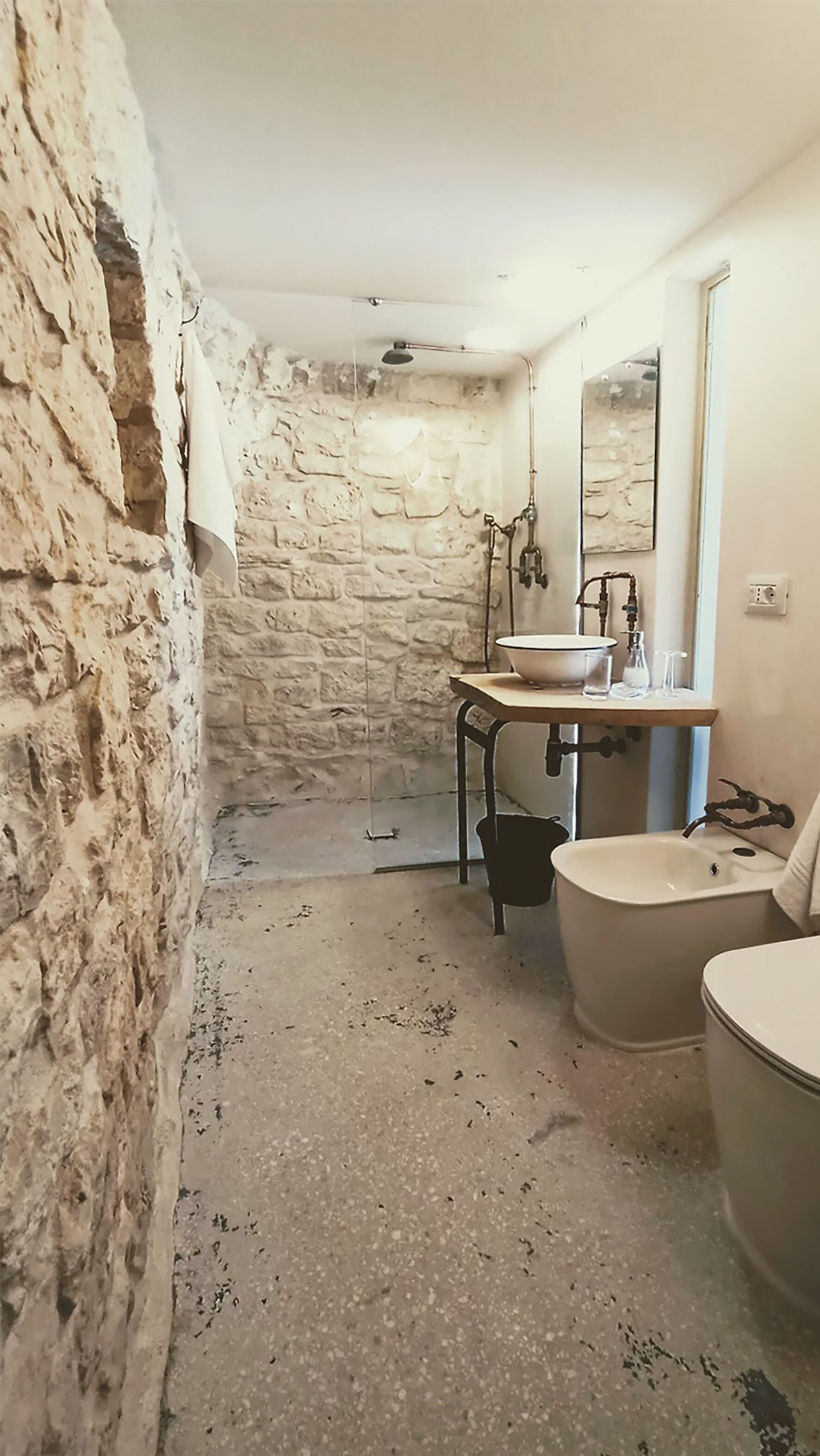 A bathroom with a stone wall, a sink, a bathtub, and a mirror.
