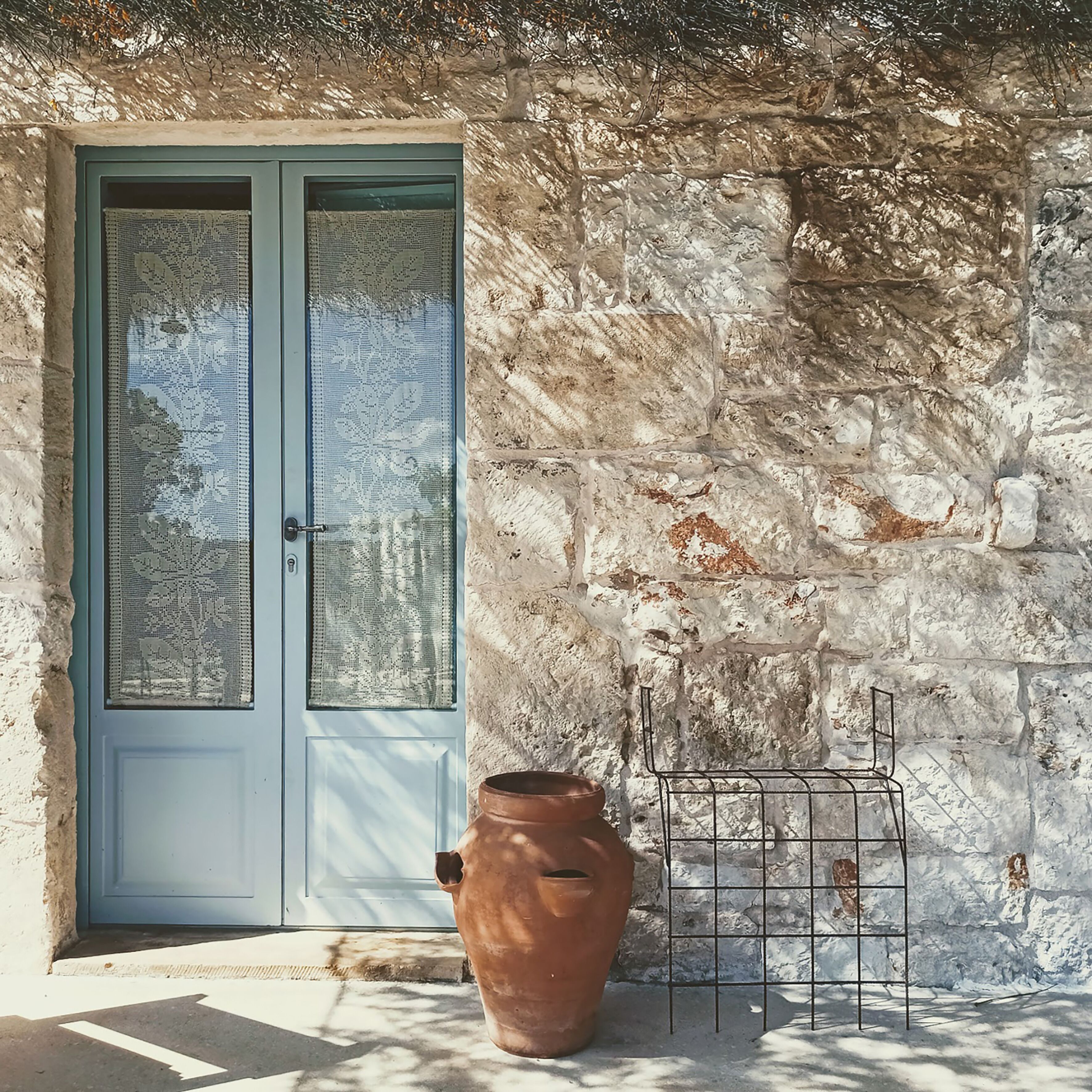 A rustic stone wall with a metal rack and a terracotta pot.