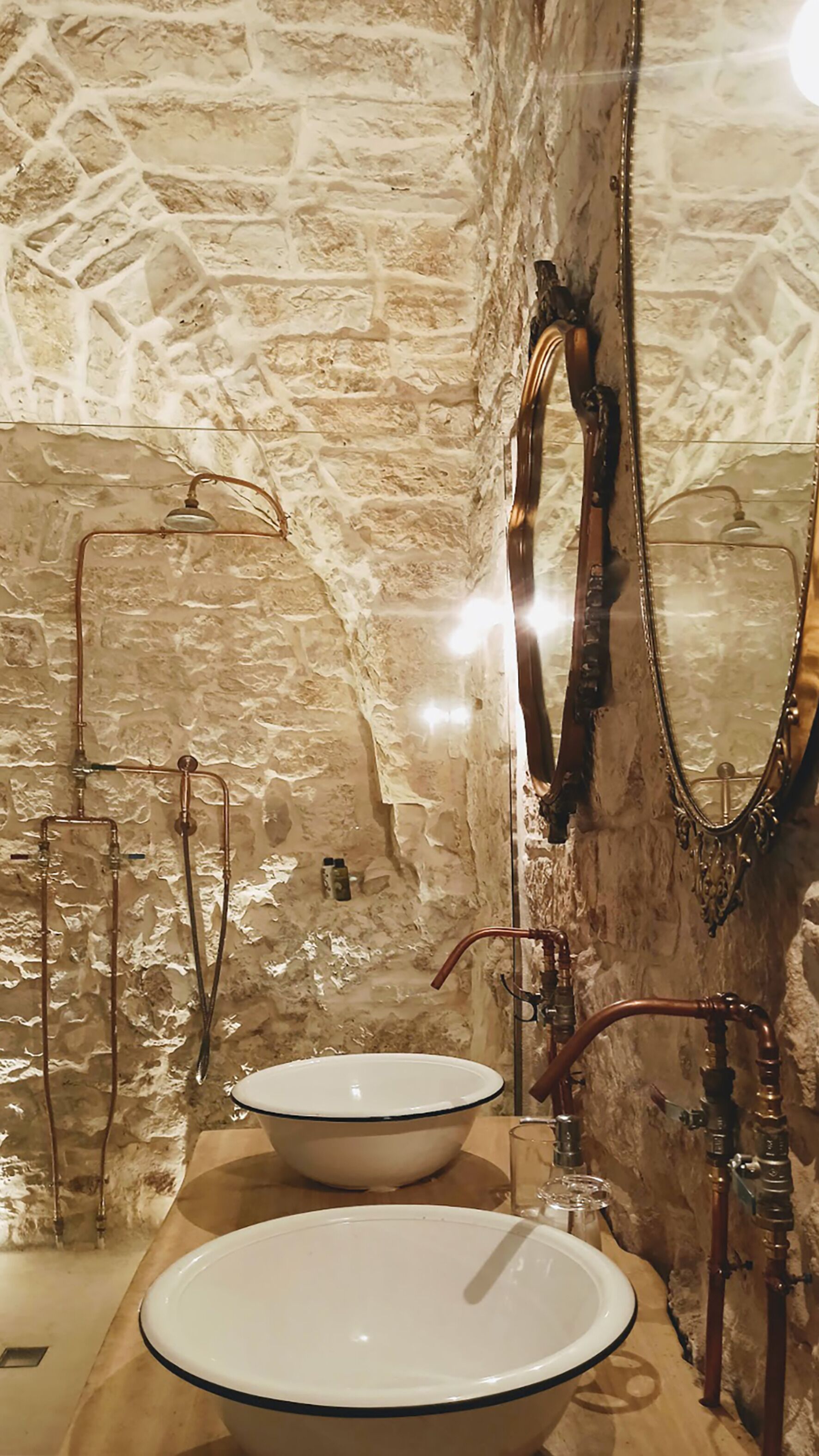 Un bagno con parete in pietra, lavabo bianco e specchio con cornice in ottone.