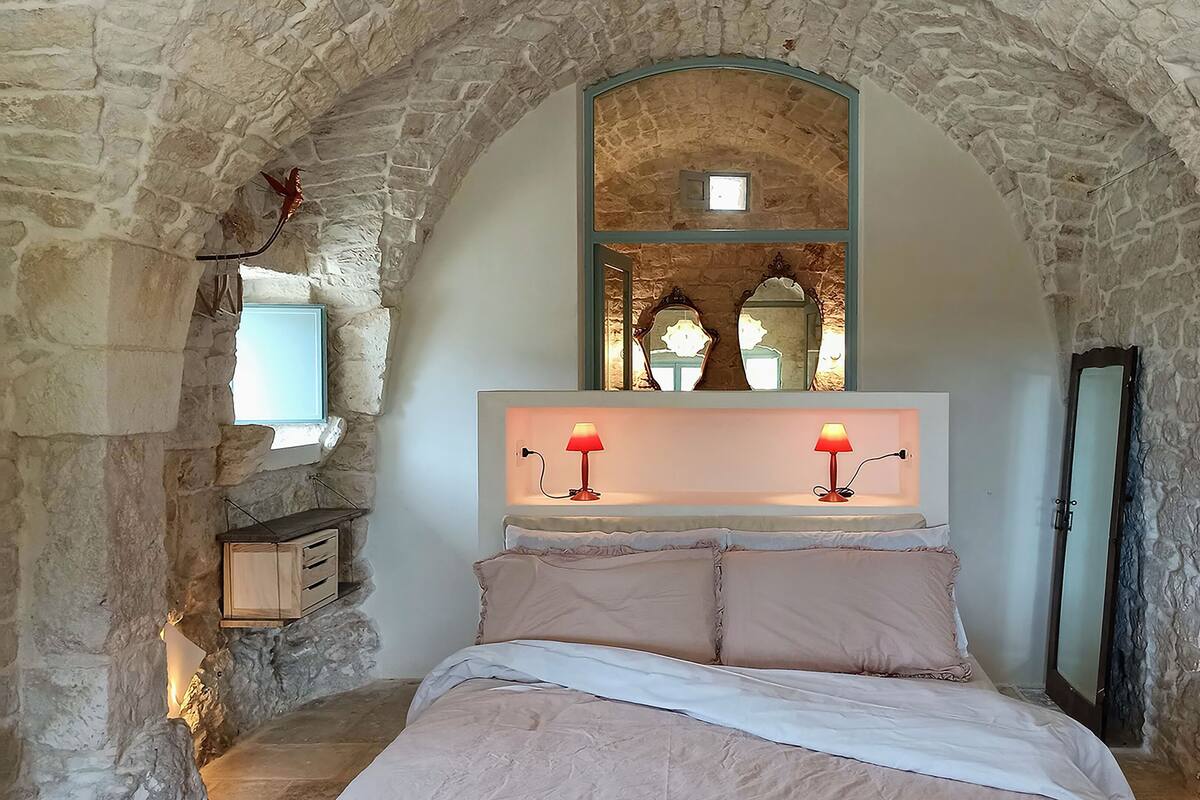 Een slaapkamer met stenen muren, een bed, een spiegel en twee wandlampen.