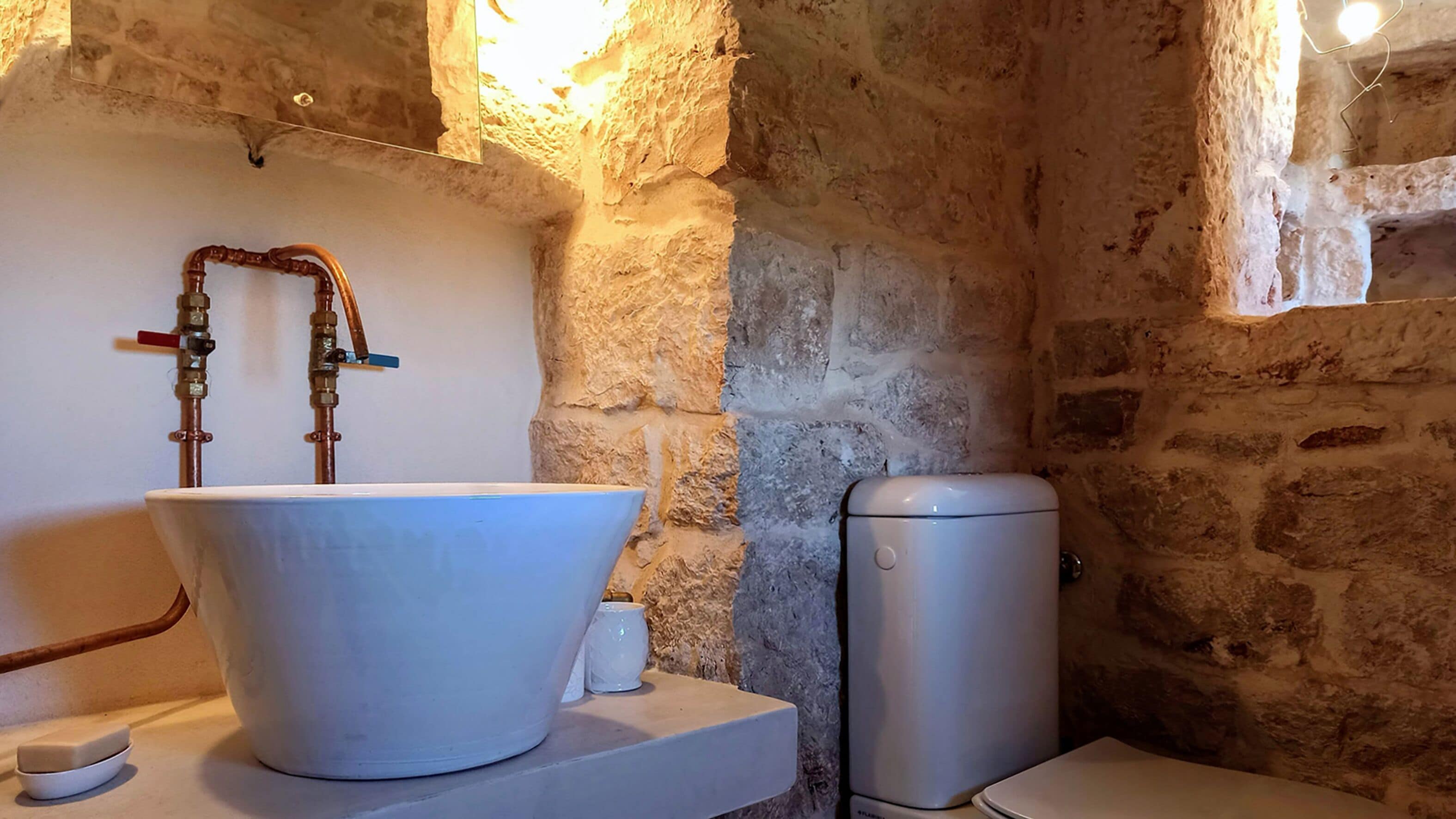 A bathroom with a large white basin, copper pipes, and a modern toilet.