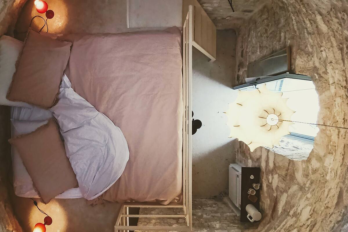 Een kamer met een bed, een klein tafeltje, een wandplank en een raam met uitzicht.