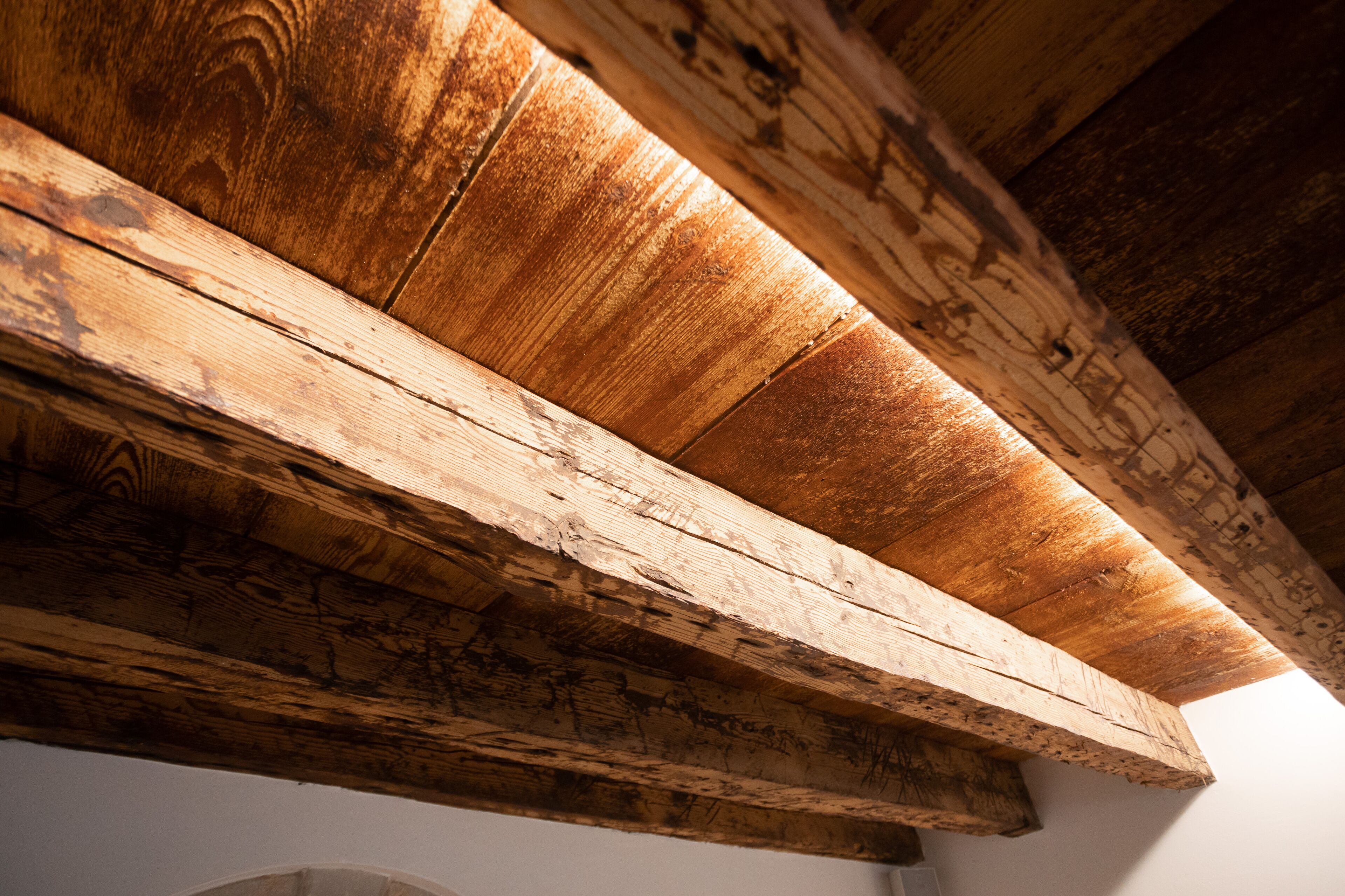 A wooden ceiling with exposed beams and a white wall.