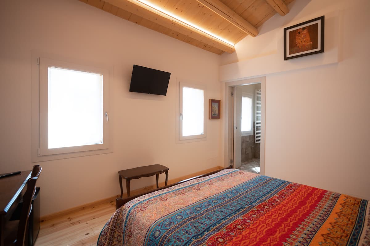 Ein Schlafzimmer mit einem Bett, einem Fernseher, einer Bank und zwei Fenstern.