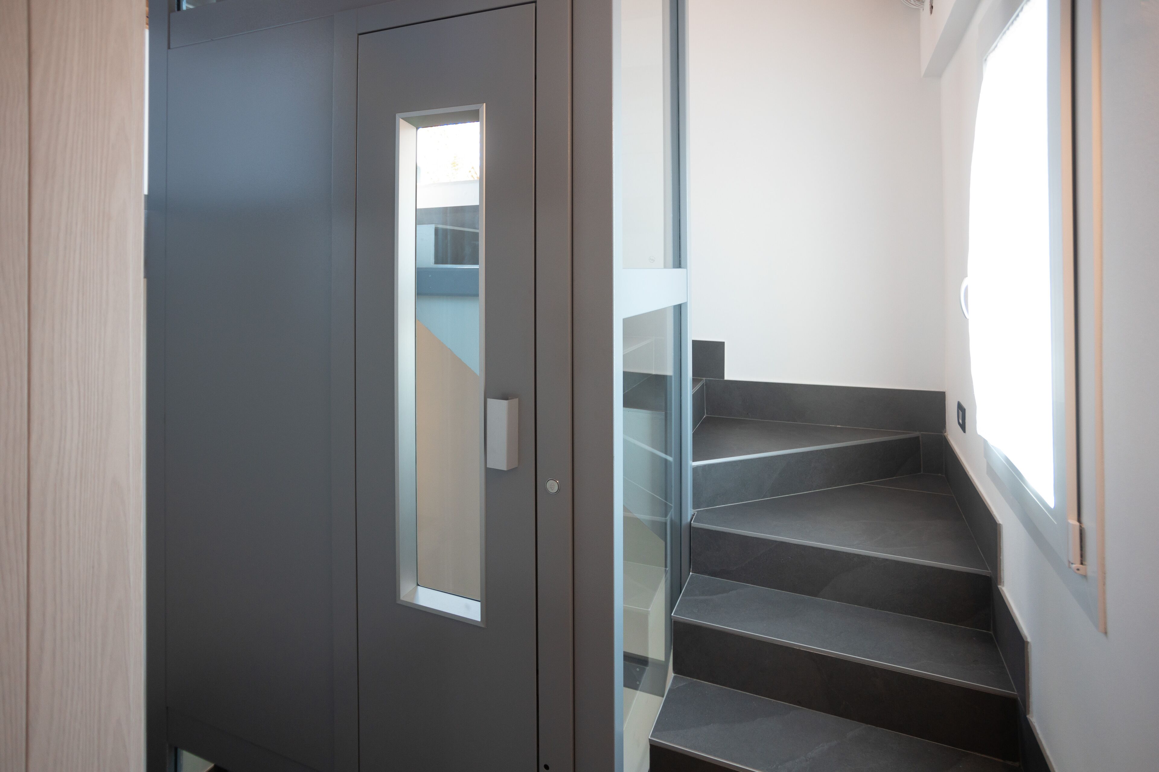 A modern staircase with dark steps and a glass railing, leading to a door with a small window.