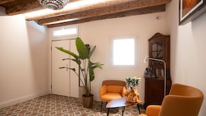 Une pièce avec des carreaux de sol à motifs, une plante en pot, deux chaises orange, une petite table avec une lampe et un meuble en bois.