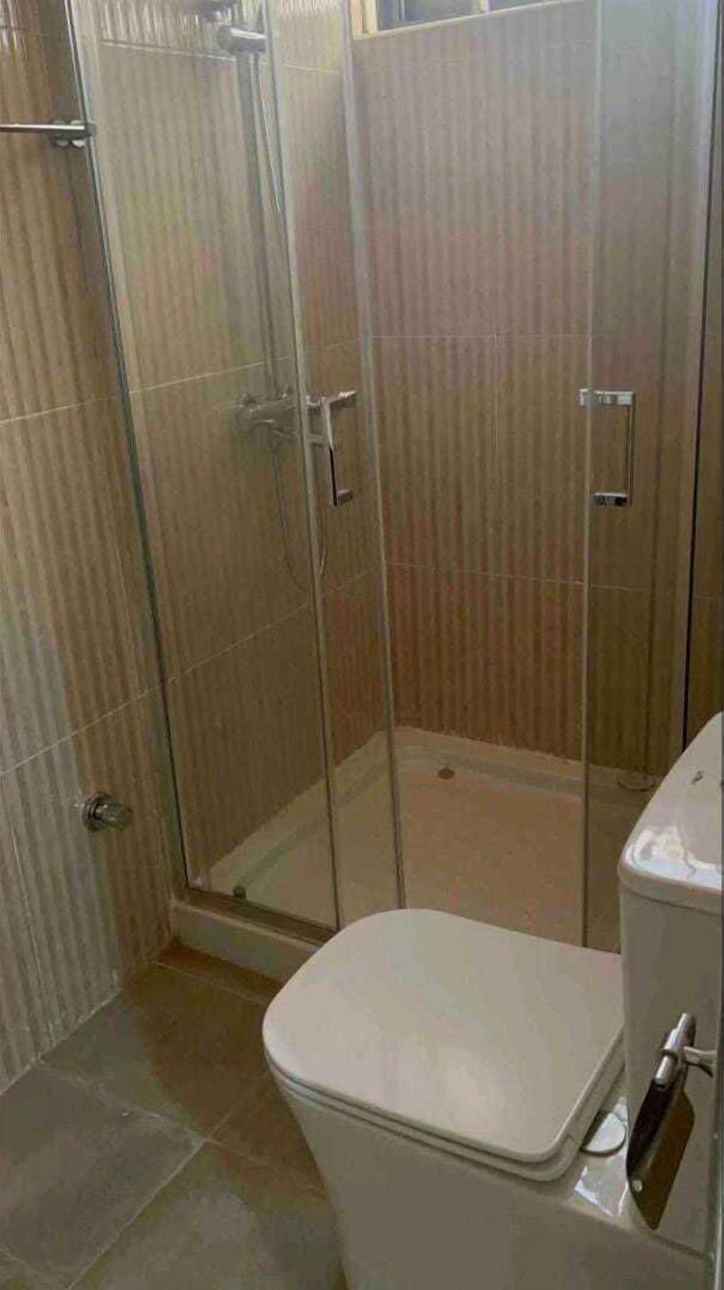 A bathroom with a glass shower enclosure, a toilet, and tiled walls.