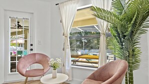 A room with two pink chairs, a small table with a vase of flowers, and a large potted plant. - Luxury Corner Home, Arcade, Heated Pool & Spa. No extra fees. Pet Friendly. (Davenport)