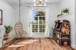 Relax in this serene space with a hanging chair and a small table, featuring a vintage arcade machine and a lush plant.