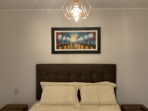 Une chambre à coucher avec un lit, un tableau encadré et un luminaire aux formes géométriques.