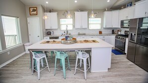 Une cuisine moderne avec des meubles blancs, un îlot central doté de tabourets, un four encastré et des luminaires suspendus.