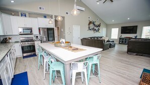 Une cuisine moderne avec des meubles blancs, un grand îlot central doté de tabourets, un ventilateur de plafond et un téléviseur à écran plat.
