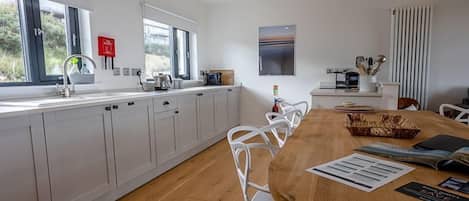 Una cocina moderna con armarios blancos, una mesa de comedor de madera y vistas al exterior a través de amplios ventanales.