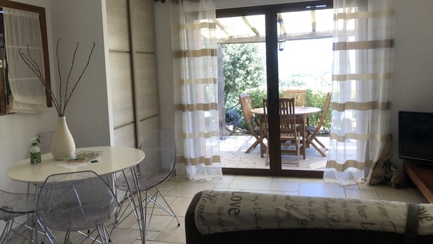Une pièce comprenant une table à manger, des chaises, un canapé, un téléviseur et une porte-fenêtre coulissante donnant sur un espace extérieur avec une table et des chaises.