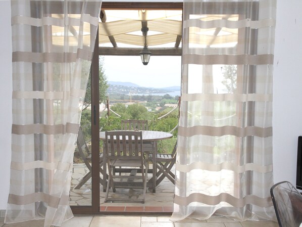 A patio with a wooden table and chairs, a view of the landscape, and a door with curtains.