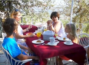 A group of people seated at an outdoor table with a red tablecloth, enjoying breakfast.