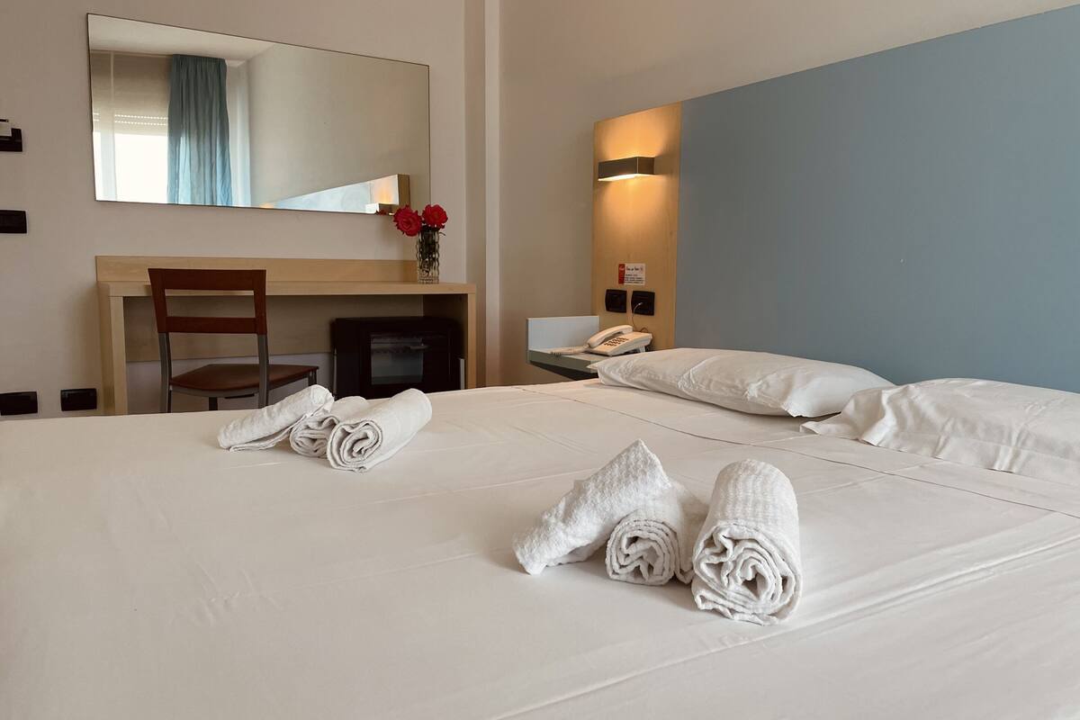 Une chambre d’hôtel avec un grand lit, une chaise, un bureau, un téléphone et un miroir.