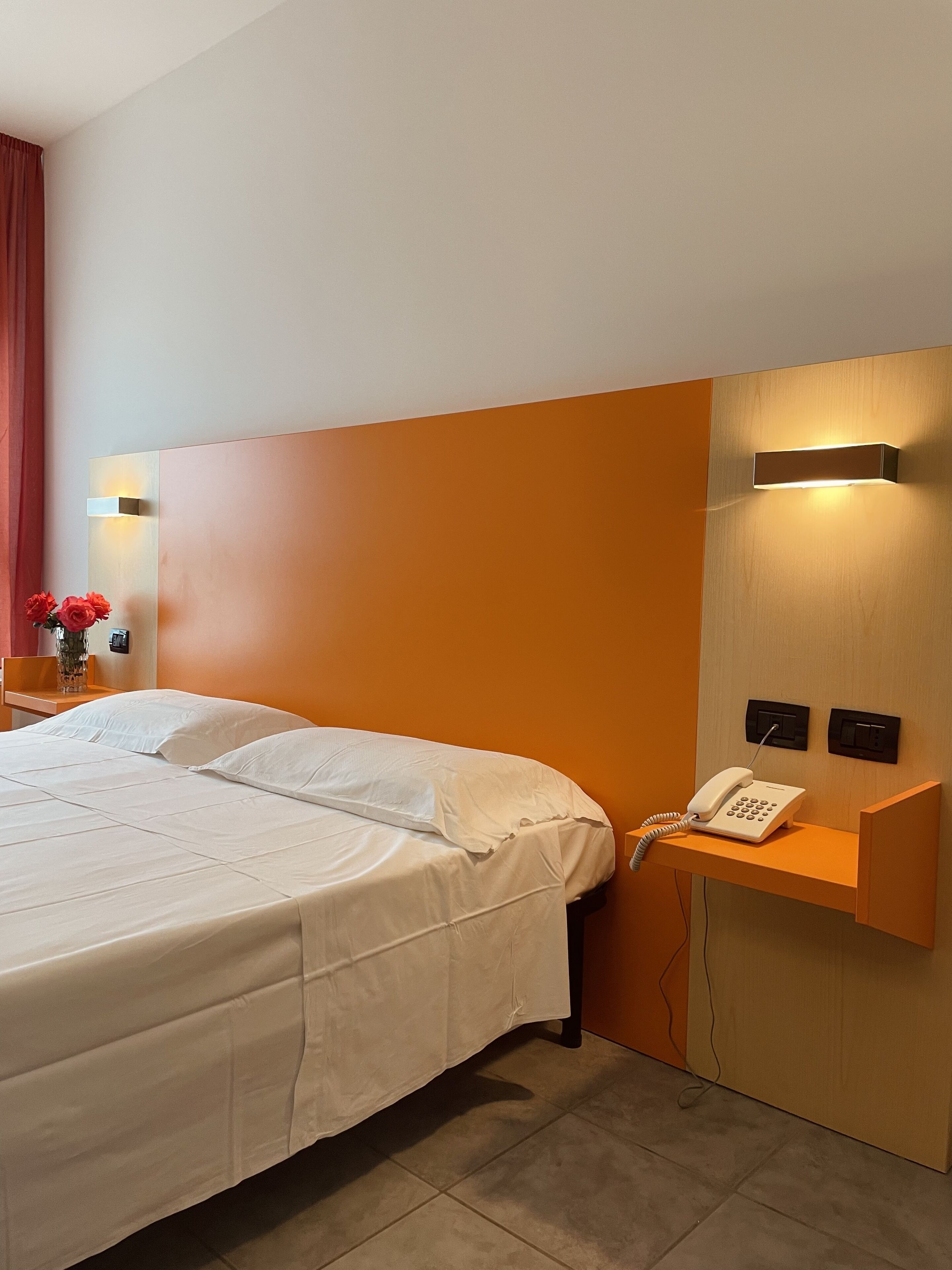 Una habitación de hotel con una cama grande, una mesita de noche con un teléfono y una lámpara de pared.