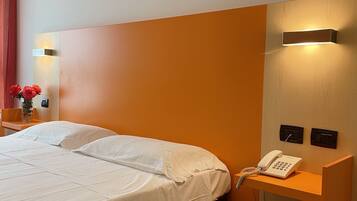 Una habitación de hotel con una cama grande, una mesita de noche con un teléfono y una lámpara de pared.