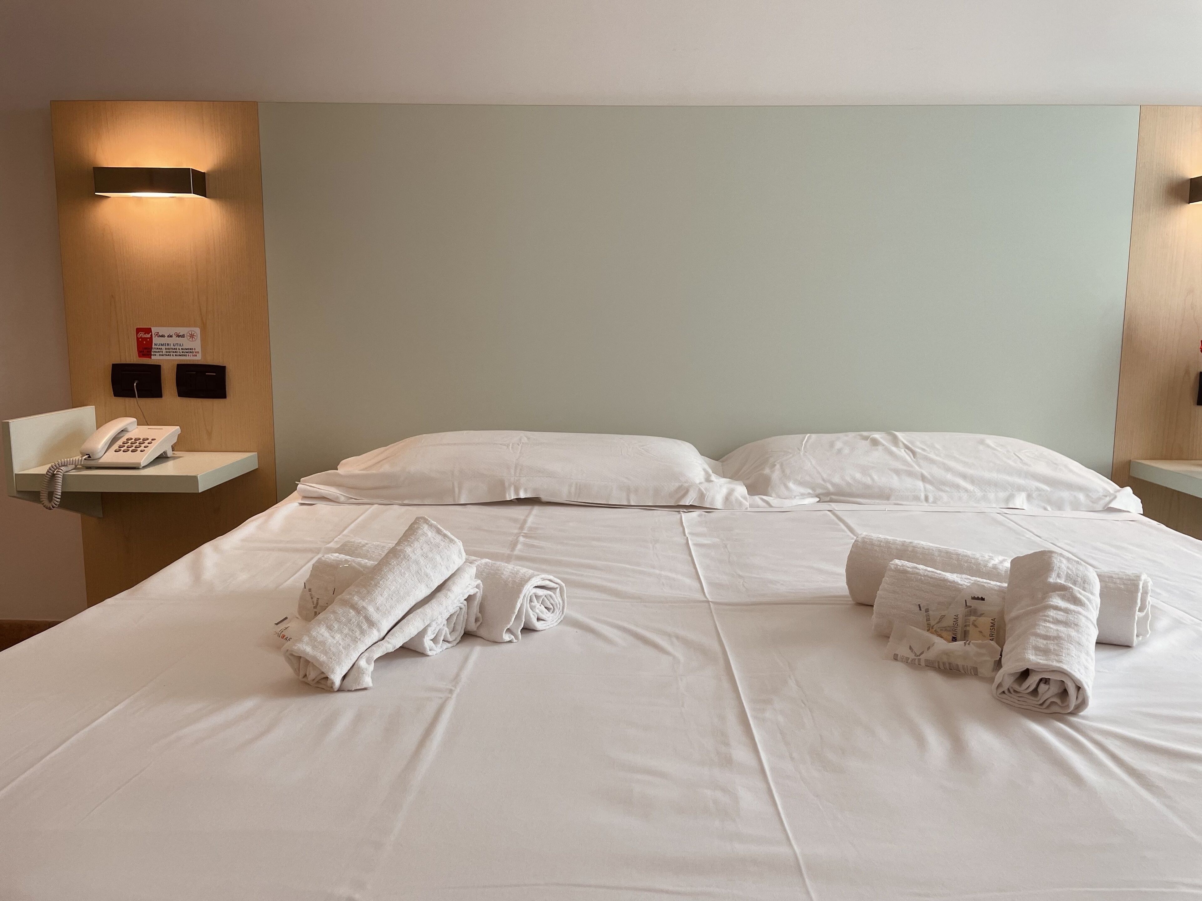 Una habitación de hotel con una cama bien hecha, un teléfono en la mesita de noche y un aplique de pared.