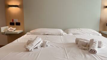 Una habitación de hotel con una cama bien hecha, un teléfono en la mesita de noche y un aplique de pared.