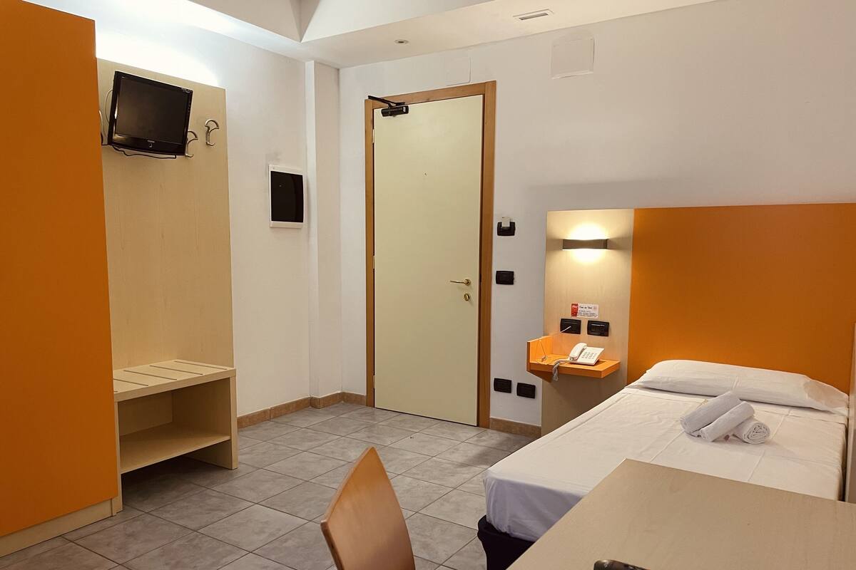 Une chambre d’hôtel équipée d’un lit, d’un bureau, d’une chaise, d’un téléviseur fixé au mur et d’un téléphone posé sur une petite étagère.