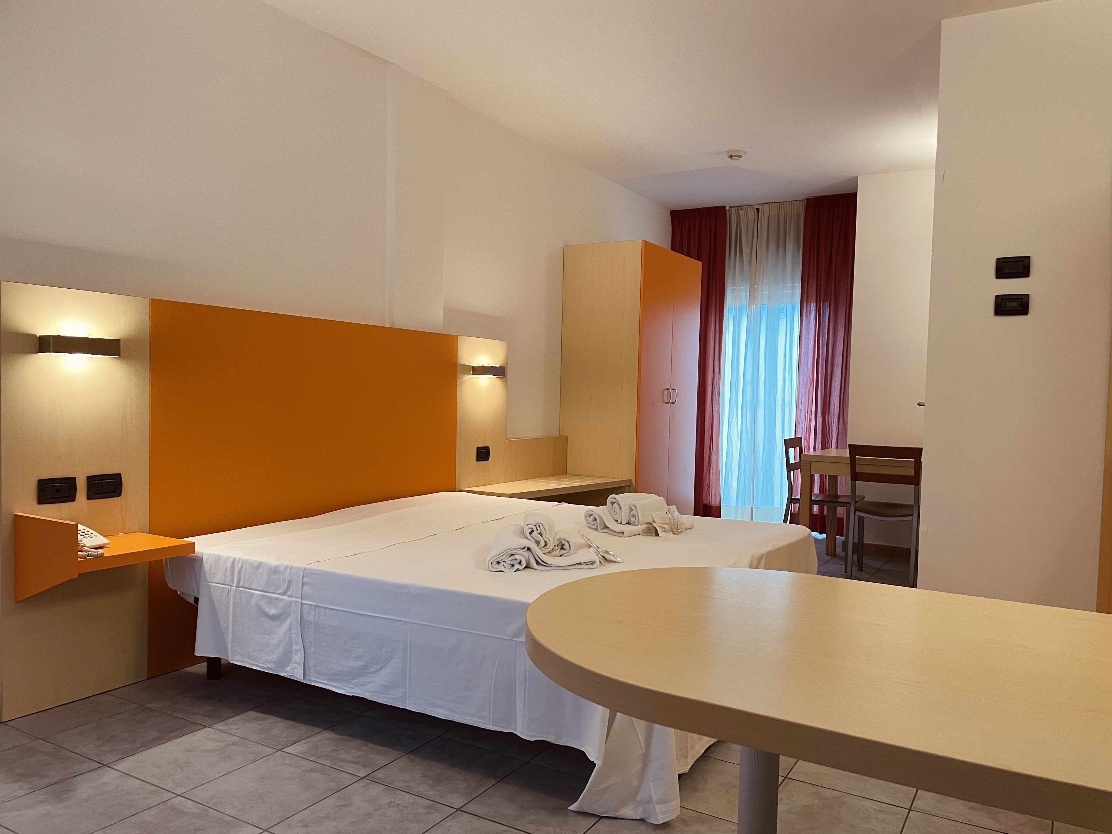 Habitació d'hotel amb un llit, un escriptori i una cadira. Hi ha dues taules de nit, una amb una làmpada i l'altra amb un telèfon.