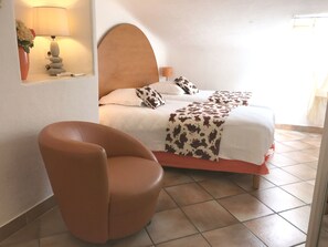 A bedroom with a bed, a chair, a lamp, and a wall-mounted shelf with a vase. - Apartment-Standard-Ensuite with Shower-Sea View-T3 (Porto-Vecchio)